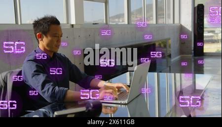 Image of multiple 5g texts over asian man sitting on chair and working on laptop in office Stock Photo
