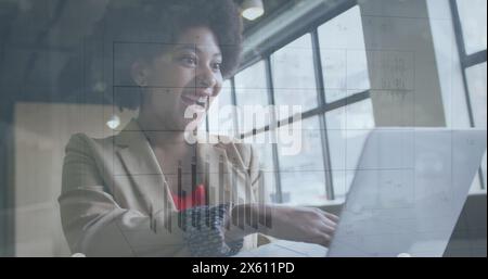 Image of changing numbers on graph over happy biracial woman scrolling on laptop Stock Photo