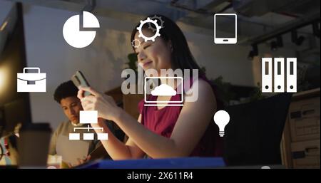 Image of computer application icons over asian businesswoman using smart phone in office Stock Photo