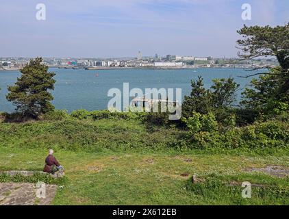 Plymouth Waterfront seen from a high vantage point on Drake’s Island with the island’s pier and foreground figure. Purchased 2019 by businessman Morga Stock Photo