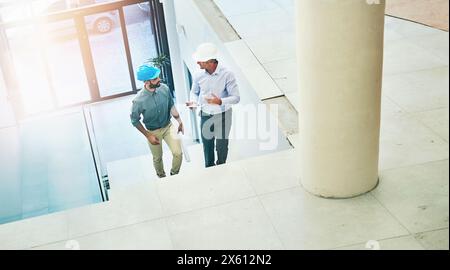 Architect, talking and businessman with hardhat in office, workplace and discussion for building design. Worker, planning and project with contractor Stock Photo