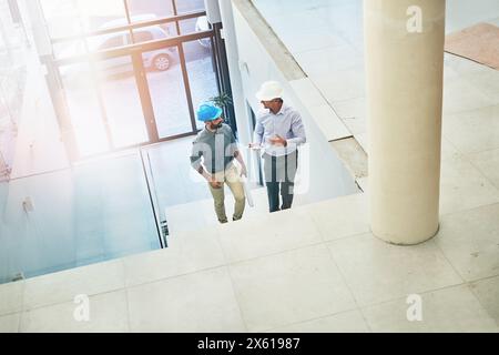 Architect, speaking and businessman with hardhat in office, workplace and discussion for building design. Worker, planning and project with contractor Stock Photo