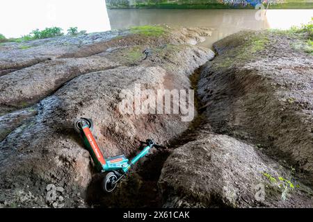 A Tier rentable e-scooter thrown onto and abandoned on the muddy bank of the River Avon in Bristol, UK. An example of Anti social Behavoir Stock Photo