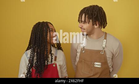 A woman and a man smiling together in aprons against a yellow background, suggesting a friendly work environment. Stock Photo