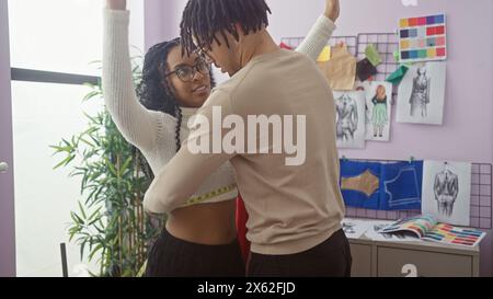 A male tailor measures a female client's waist in a design room filled with fashion sketches and fabric swatches. Stock Photo