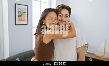 An interracial couple hugs lovingly in a cozy living room, showcasing harmony and affection. Stock Photo