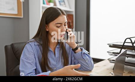 A professional hispanic woman converses on the phone in a modern office setting, exuding concentration and business acumen. Stock Photo