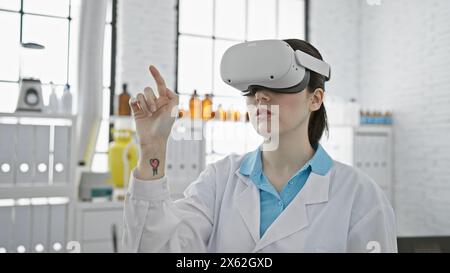 A young caucasian woman in a lab coat uses vr technology indoors at a modern laboratory. Stock Photo