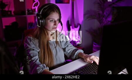 Focused young woman gaming in a dark room with purple backlighting, wearing headphones. Stock Photo