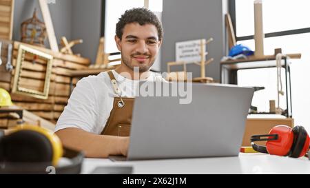 Smiling craftsman using laptop in a well-organized modern carpentry workshop Stock Photo