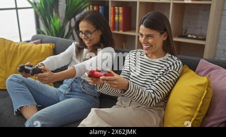 A mother and daughter enjoy playing video games together on a cozy sofa in a modern living room, sharing a joyful moment. Stock Photo