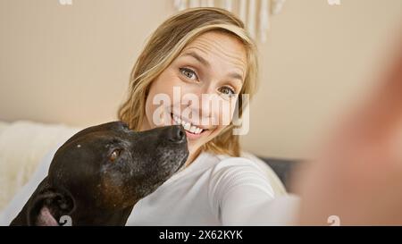 Smiling caucasian woman taking a selfie with her affectionate black dog in a cozy living room. Stock Photo