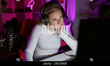 Focused young woman gaming at night with headset and microphone in a colorful room Stock Photo