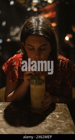 Cheerful, beautiful hispanic woman enjoying a tropical cocktail drink in a lively nightclub, embodying the essence of fun-filled nightlife. Stock Photo