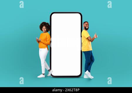 Smiling Black Man and Woman Standing Beside a Giant Smartphone Stock Photo