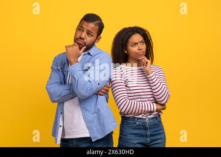 Pensive Young Couple Standing Back to Back Against Yellow Background Stock Photo