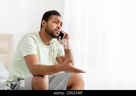 Young Man Sitting on Bed, Engaged in Phone Conversation Stock Photo