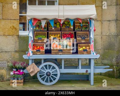 Blue wooden hand cart decorated with red white and blue bunting, displaying boxes of fruit and vegetables. Stock Photo