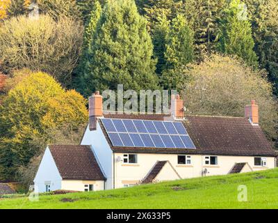 Solar panels on a white cottage, nestled against a hill in the foreground with the autumn-coloured backdrop of Dalby Forest. North Yorkshire, UK Stock Photo