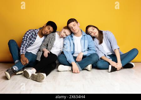 Young Friends Sitting Together and Resting Against a Yellow Wall Stock Photo