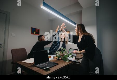 Diverse office team celebrates success with a high-five in a modern workspace Stock Photo