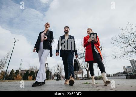 Three business professionals walking outdoors in an urban setting, engaged in conversation Stock Photo