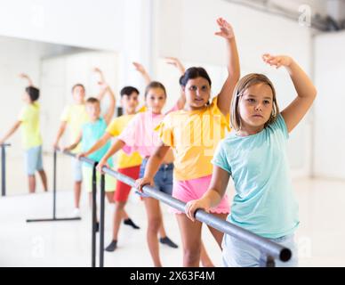 Focused tween girl practicing ballet positions near bar during group class Stock Photo