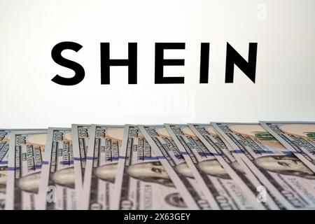 SHEIN logo seen on the screen and dollar banknotes near it. Stafford, United Kingdom, April 28, 2024 Stock Photo