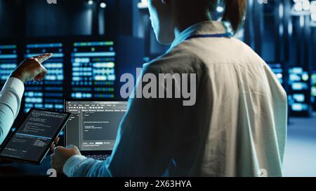 Engineering team members running code on tablet and laptop, updating professional data center equipment designed to accommodate server rigs, networking systems and storage arrays Stock Photo