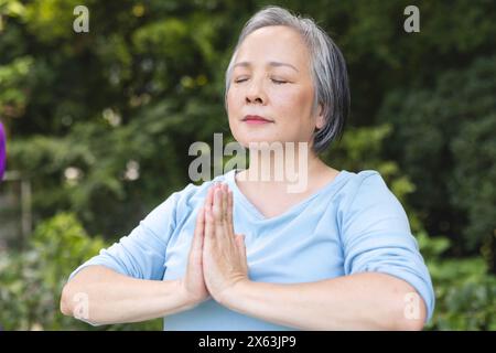 Practicing yoga outdoors, senior Asian female wearing a light blue top Stock Photo