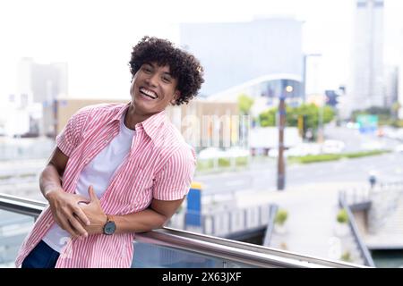 In modern office, biracial young man leaning on railing, smiling, copy space Stock Photo