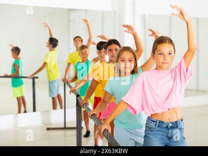Focused tween girl practicing ballet positions near bar during group class Stock Photo