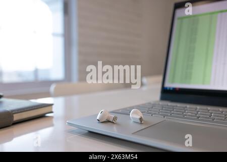 In the office, laptop shows spreadsheet; wireless earbuds rest on touchpad Stock Photo