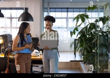 At office, diverse female business colleagues holding laptop, discussing work Stock Photo