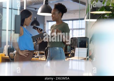 At office, diverse female business colleagues discussing work, holding tablets Stock Photo