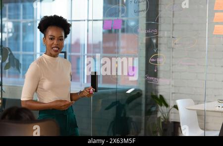 At office, African American businesswoman presenting, holding smartphone Stock Photo