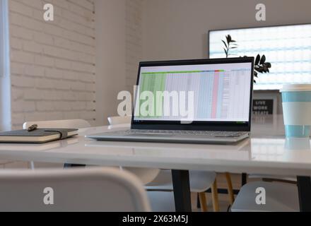 At office, laptop on white desk displaying spreadsheet, notebook beside it Stock Photo