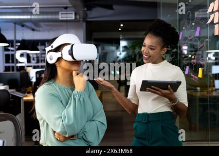 Diverse female colleagues work late using VR and tablets, with black background Stock Photo