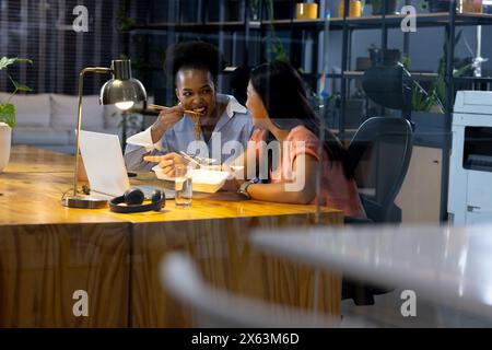At office, diverse female business colleagues eating, discussing, working late Stock Photo