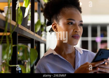 At office, African American businesswoman holding smartphone, working late Stock Photo