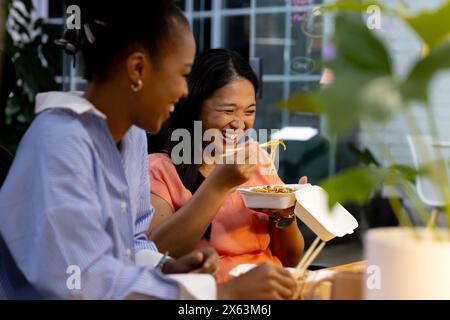 At office, diverse female business colleagues enjoying meal together, working late Stock Photo