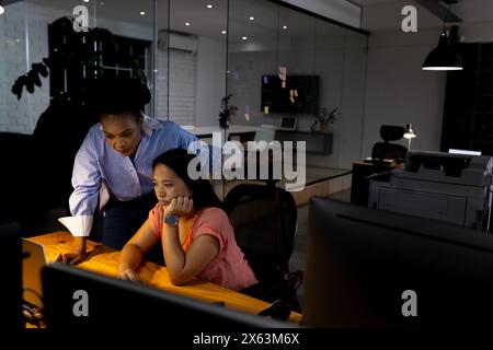 Diverse female business colleagues discussing over computer, working late Stock Photo