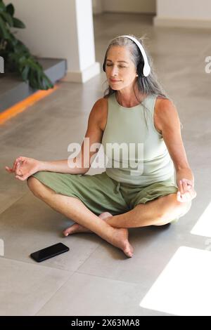 At home, Caucasian mature woman meditating with headphones Stock Photo