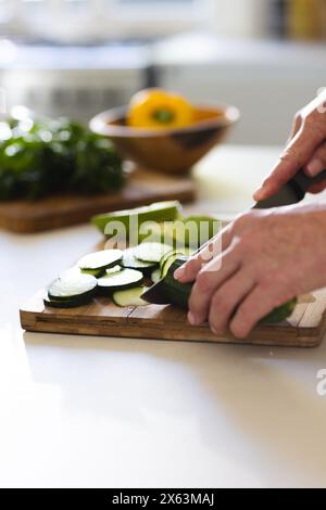 At home, mature Caucasian woman slicing zucchini on a wooden board Stock Photo