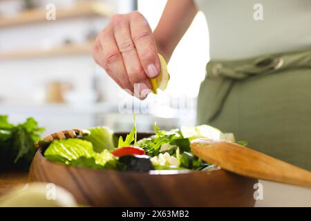 At home, mature caucasian woman squeezing lemon juice over salad Stock Photo