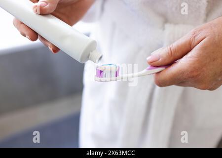At home, mature Caucasian woman putting toothpaste on toothbrush Stock Photo