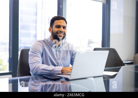 A biracial young professional man, sitting at office desk, typing on laptop Stock Photo