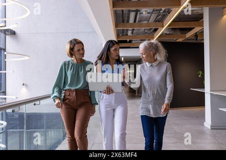 A diverse team at office, walking and discussing, carrying laptops Stock Photo