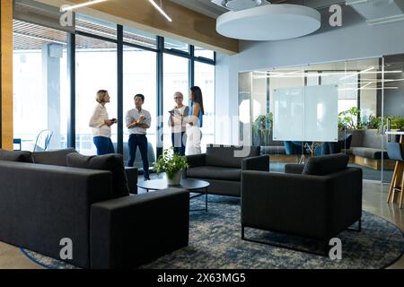 Diverse team standing, talking in modern office lounge, copy space Stock Photo