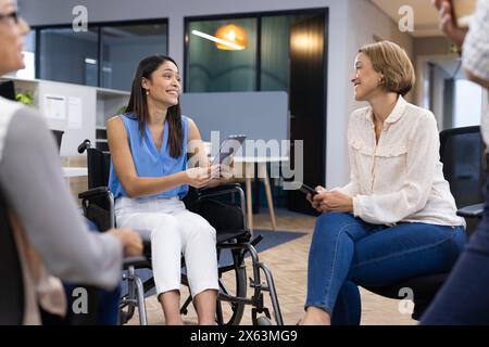 Diverse team discussing at office, one in wheelchair, holding tablets Stock Photo
